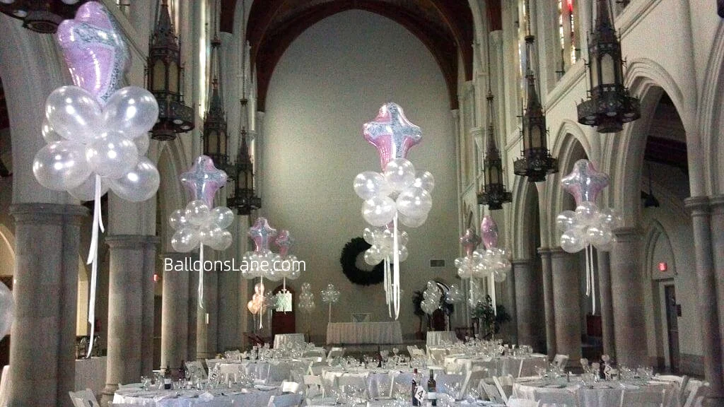 Large cross-shaped communion balloons by Balloons Lane, accompanied by clear floating balloons, celebrating a baptism in Brooklyn.