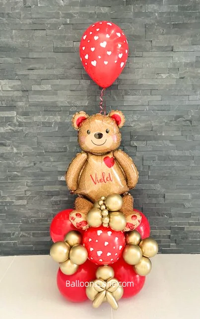 A festive balloon arrangement featuring a heart-printed red latex foil balloon, accompanied by a cute bear foil balloon, and complemented with gold and red latex balloons, set in New Jersey.