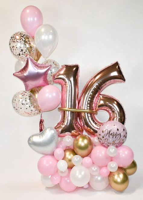 A bouquet featuring a rose gold number 16 balloon, pink heart balloon, white heart balloon, and multiple-sized pink, white, and gold balloons, in NYC.