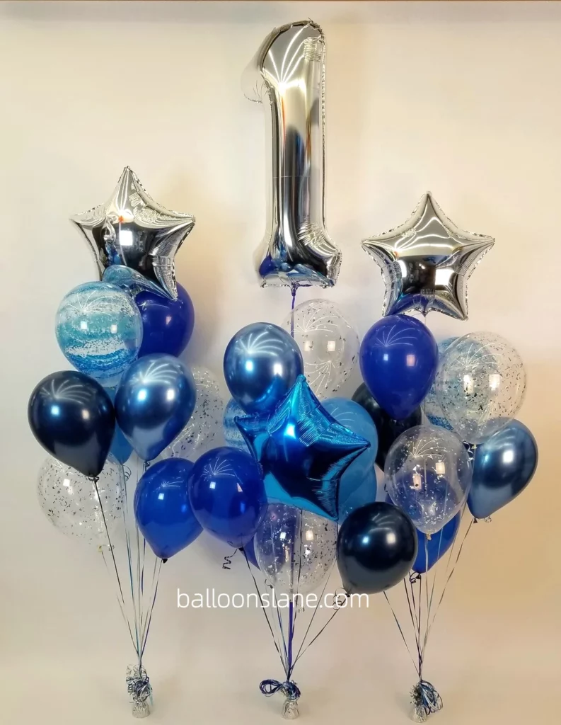 One large silver balloon accompanied by a silver star balloon, blue star balloon, blue chrome balloon, blue latex balloon, and blue confetti balloon to celebrate a 1st birthday in NJ.