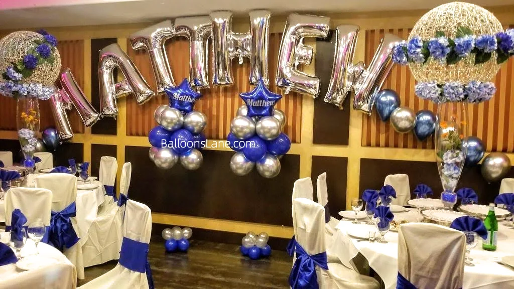 Silver letters balloons forming an arch, adorned with blue star foil balloons and clusters of blue and silver latex balloons.